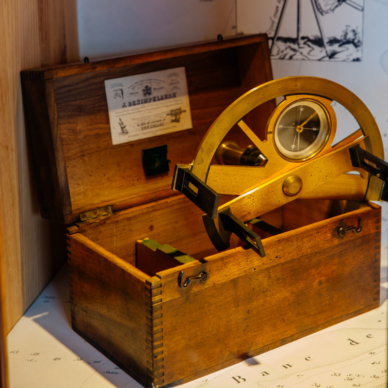 Présentant l’exposition sur l’évolution de la cartographie marine : anciennes et nouvelles cartes, table tactile interactive et instruments de navigation utilisés pour guider les marins.
