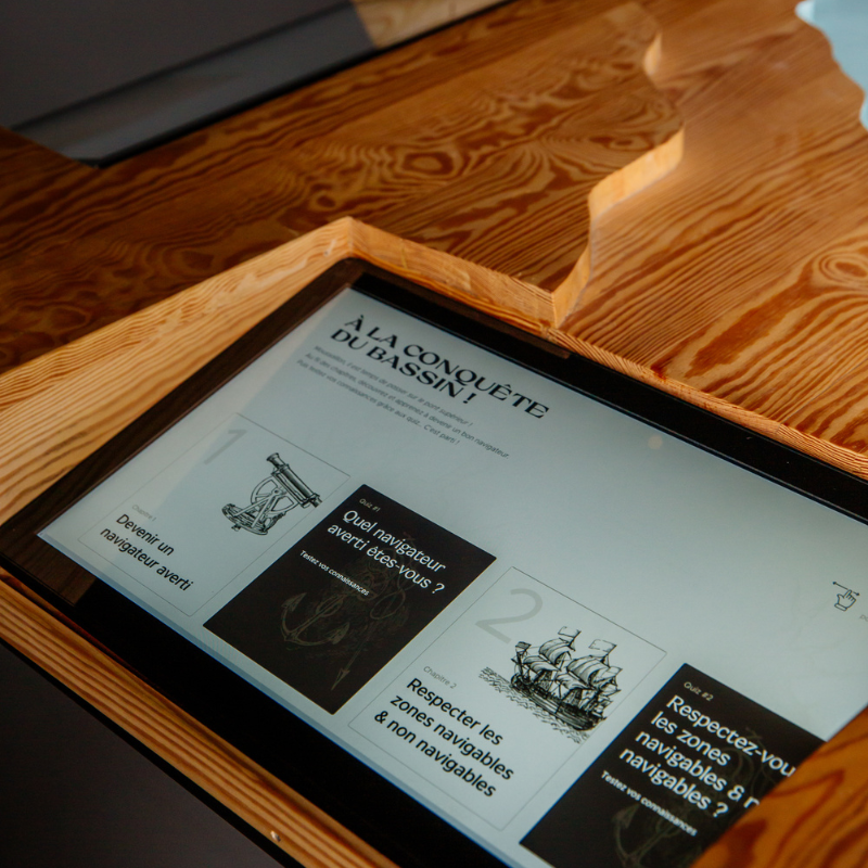 Borne interactive de la Salle de Navigation du Phare du Cap Ferret, permettant aux visiteurs d’explorer le Bassin d’Arcachon à travers quizz, cartes et applications pédagogiques.